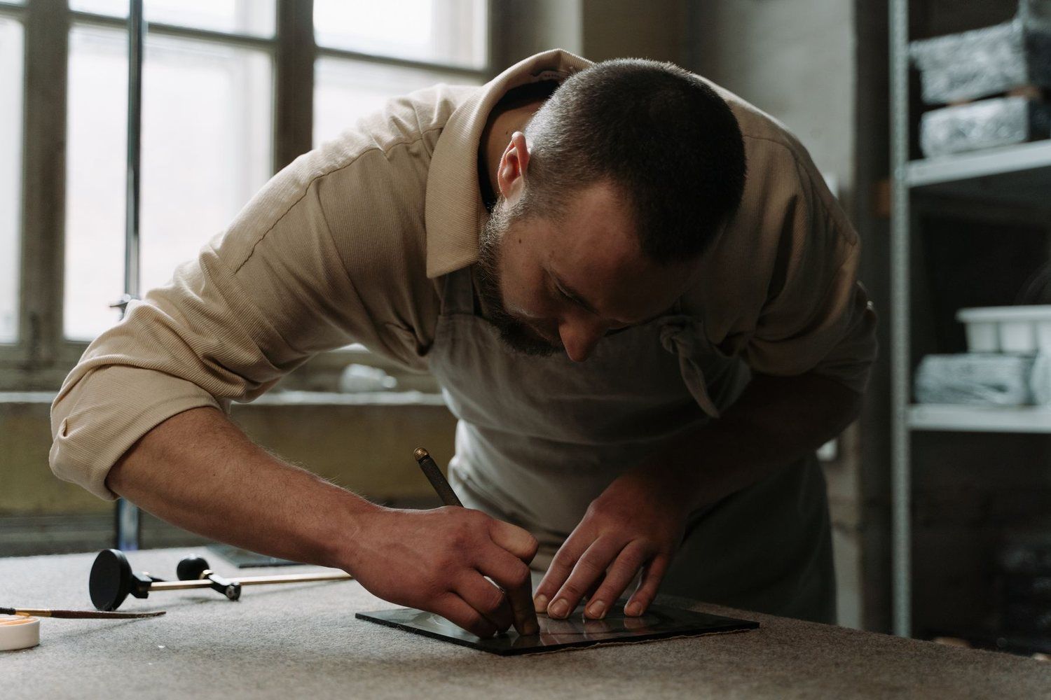 Meșter care taie sticlă la dimensiune pe masa din atelier