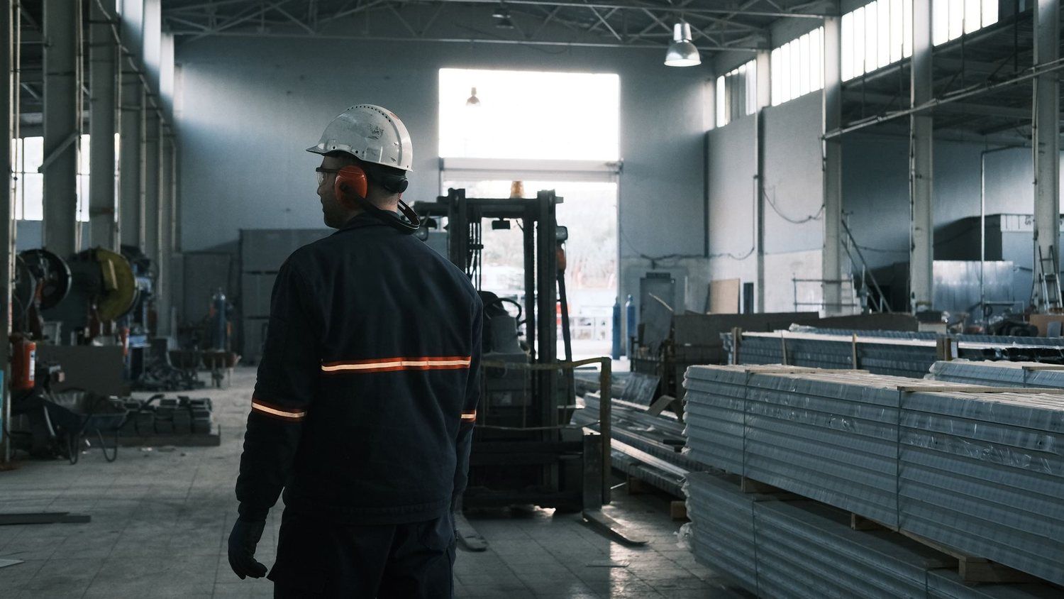 Muncitor cu cască de protecție într-o hală de producție, lângă stive de profile