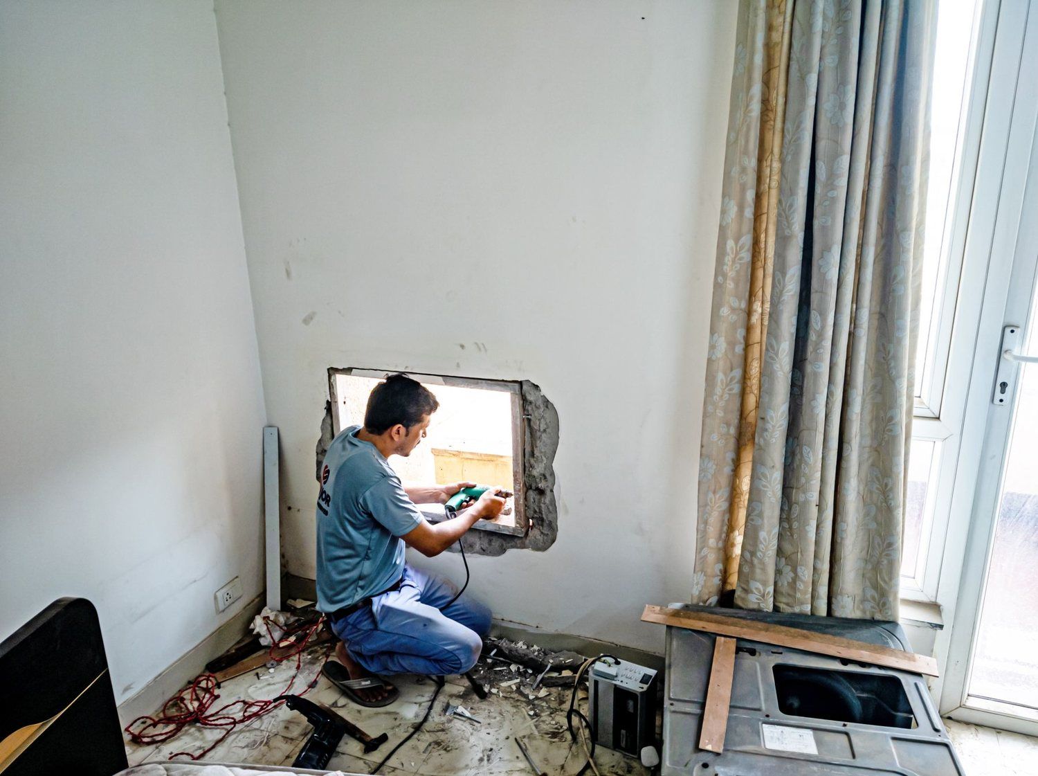 Montator care lucrează cu bormașina la golul unei ferestre, într-o cameră în renovare